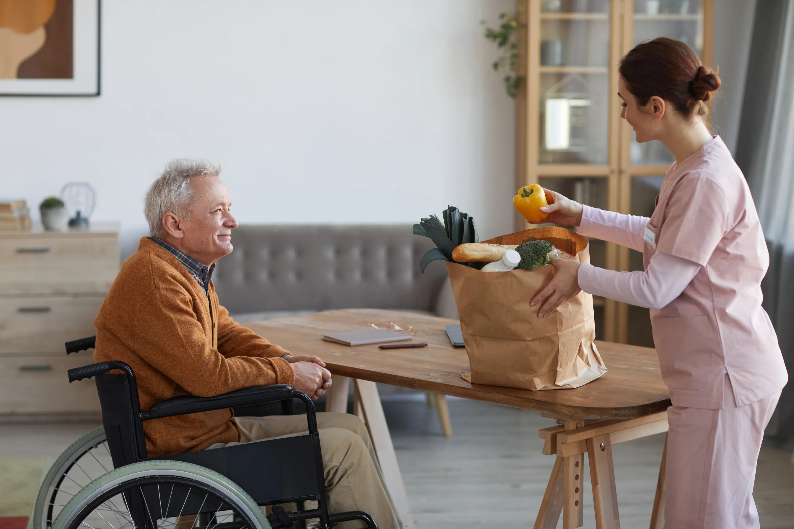 Caregiver bringing groceries to a man in a wheelchair