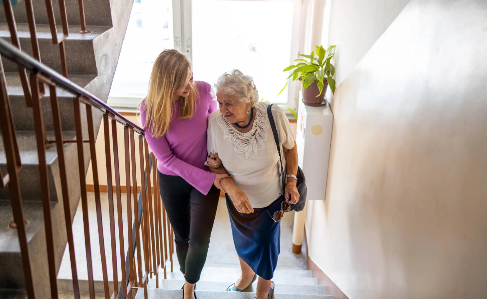 Caregiver helping an older woman up the stairs at home