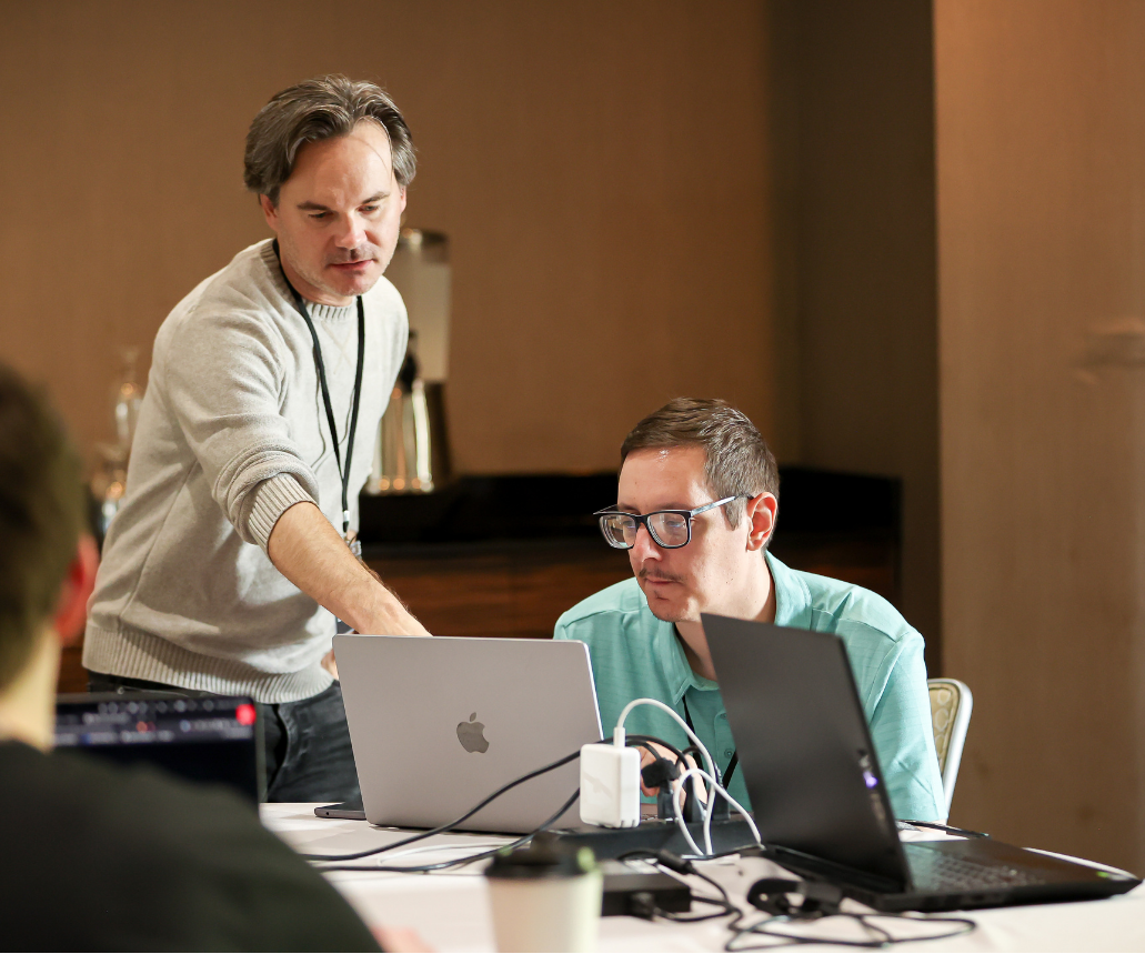 Two men collaborating at laptops during a tech training or development session.