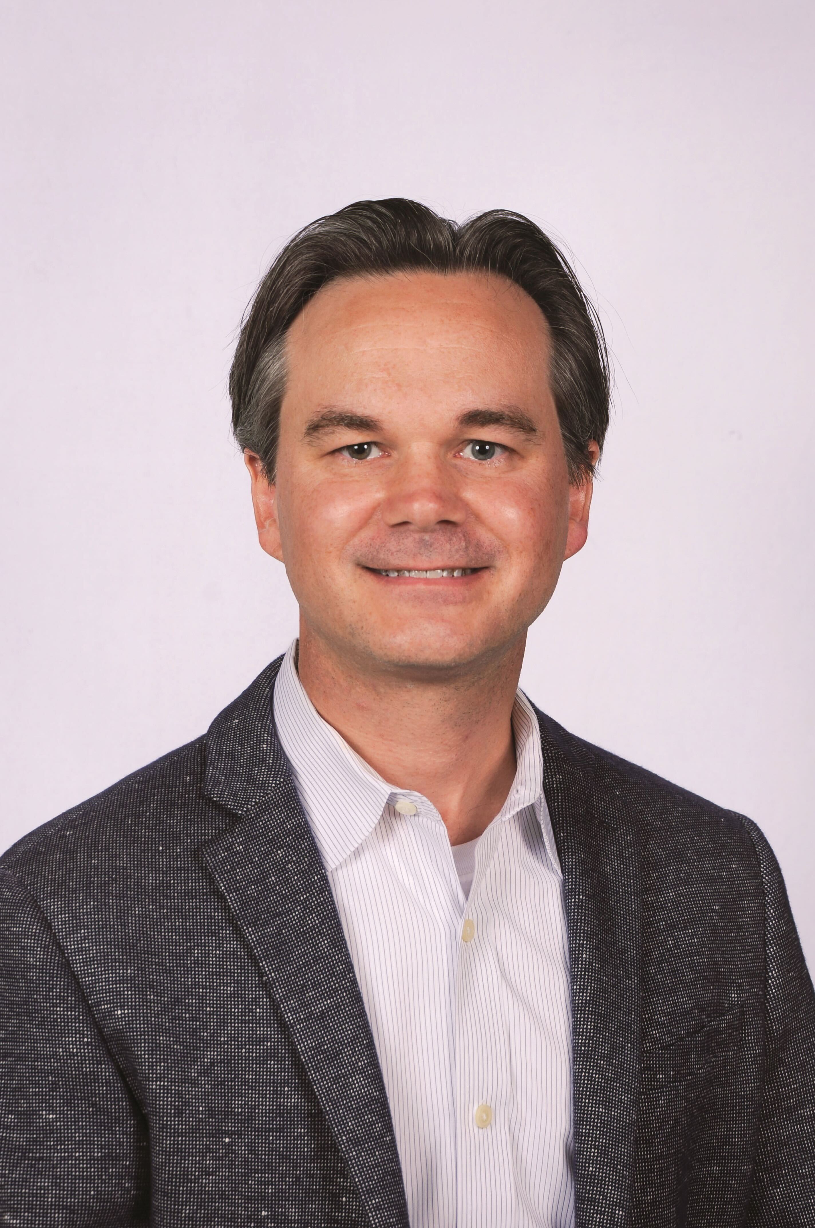 Professional headshot of middle-aged man in dark blazer and striped shirt.
