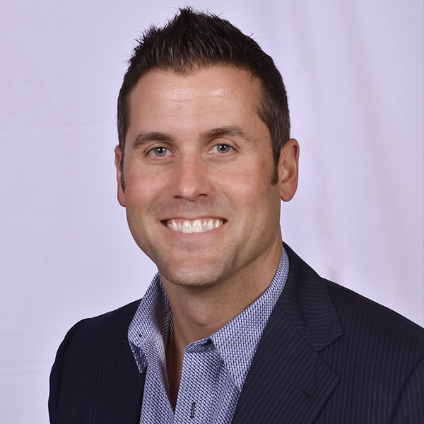 Smiling man in dark blazer and blue checkered shirt, professional headshot.