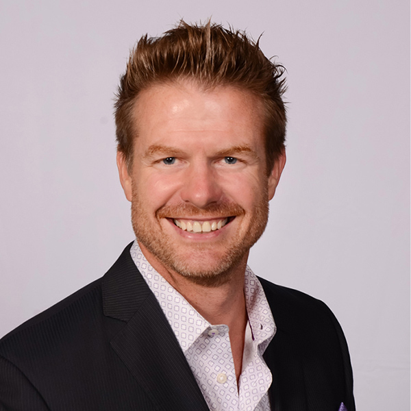 Smiling man with spiky brown hair wearing black blazer and pink shirt