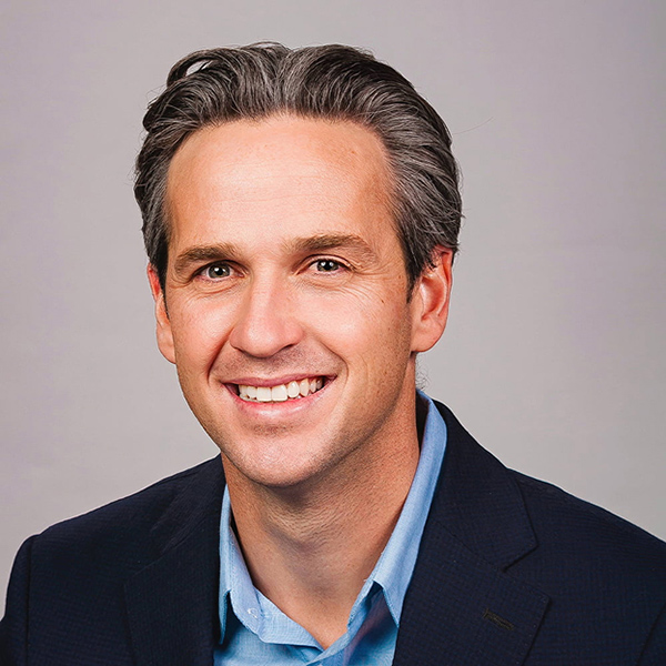 Professional headshot of a smiling middle-aged man in dark blazer and blue shirt