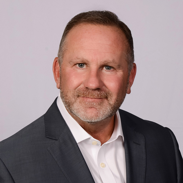 Middle-aged man in dark blazer and white shirt against gray background
