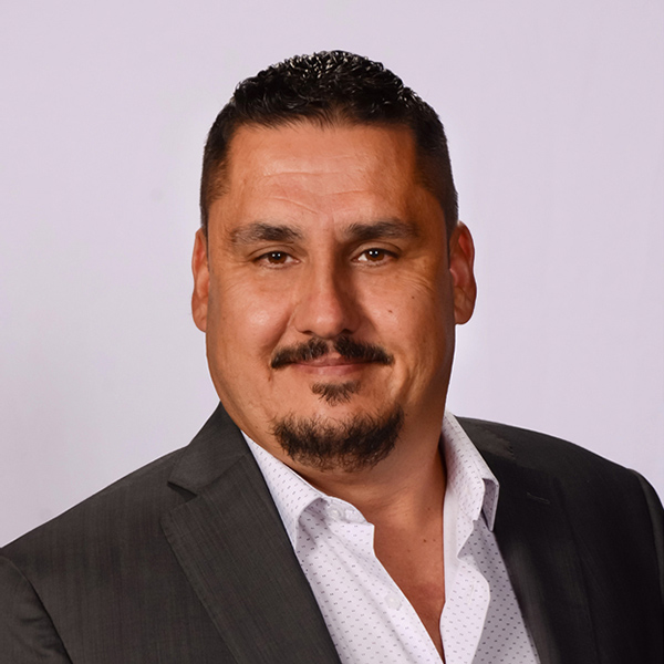 Portrait of man with dark hair and mustache wearing black blazer, light purple background