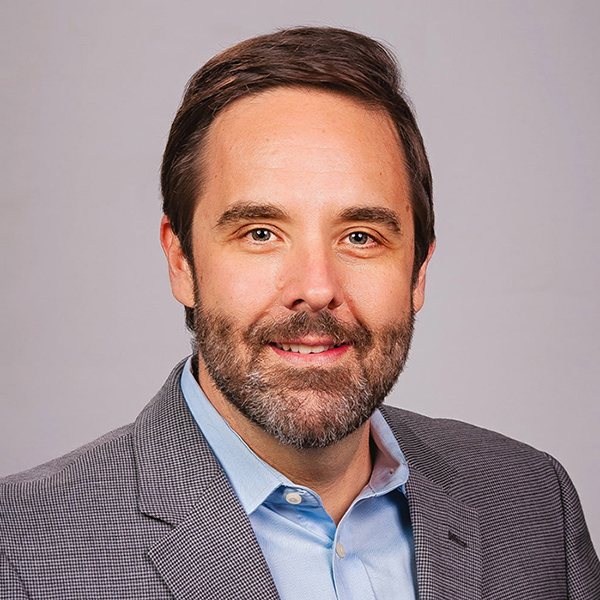 Professional headshot of smiling bearded man wearing gray blazer and blue shirt