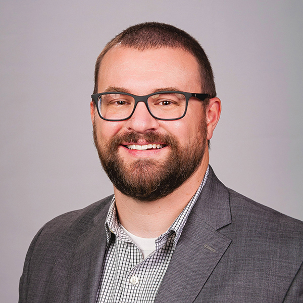 Smiling man with beard wearing glasses and dark blazer