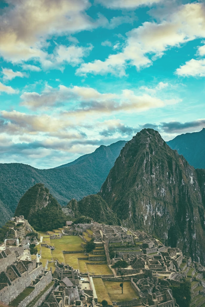 Ancient stone ruins of Machu Picchu with green terraces and surrounding mountains under a partly cloudy sky.