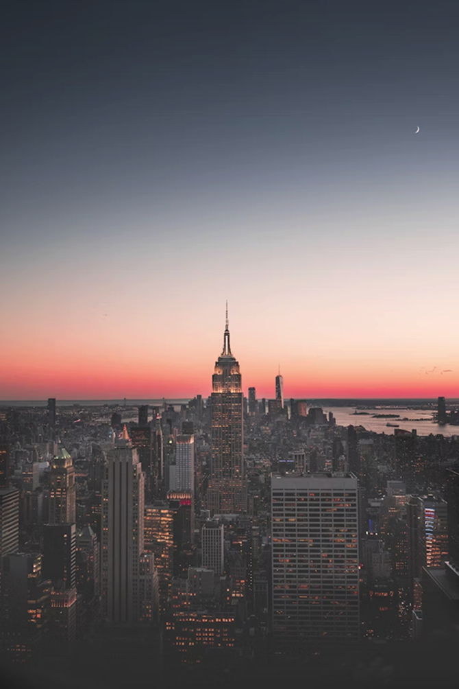 New York City skyline at dusk with the Empire State Building illuminated under a gradient sky and crescent moon.