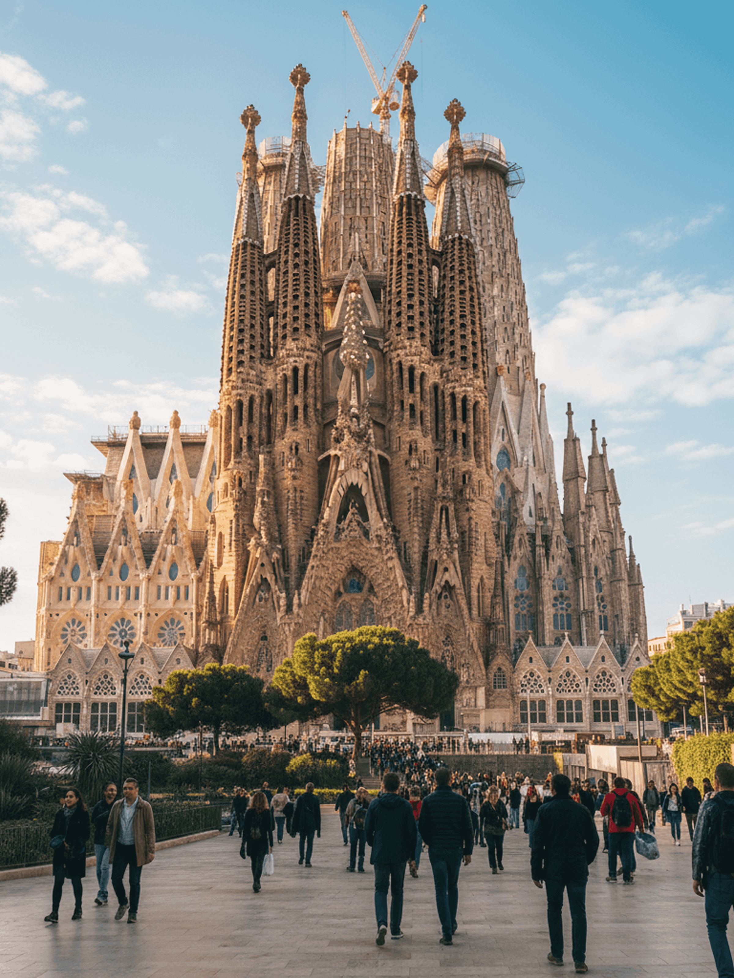 Tourists walking toward the Sagrada Família basilica in Barcelona under a clear blue sky.