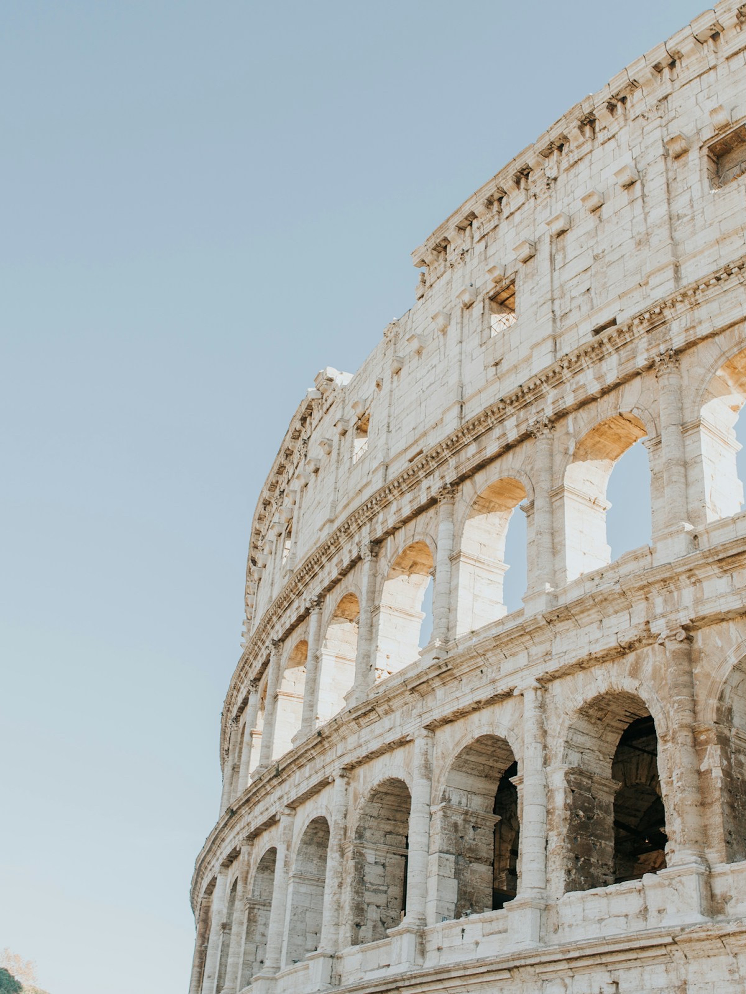 Close-up angled view of the Colosseum's ancient stone arches against a clear blue sky.