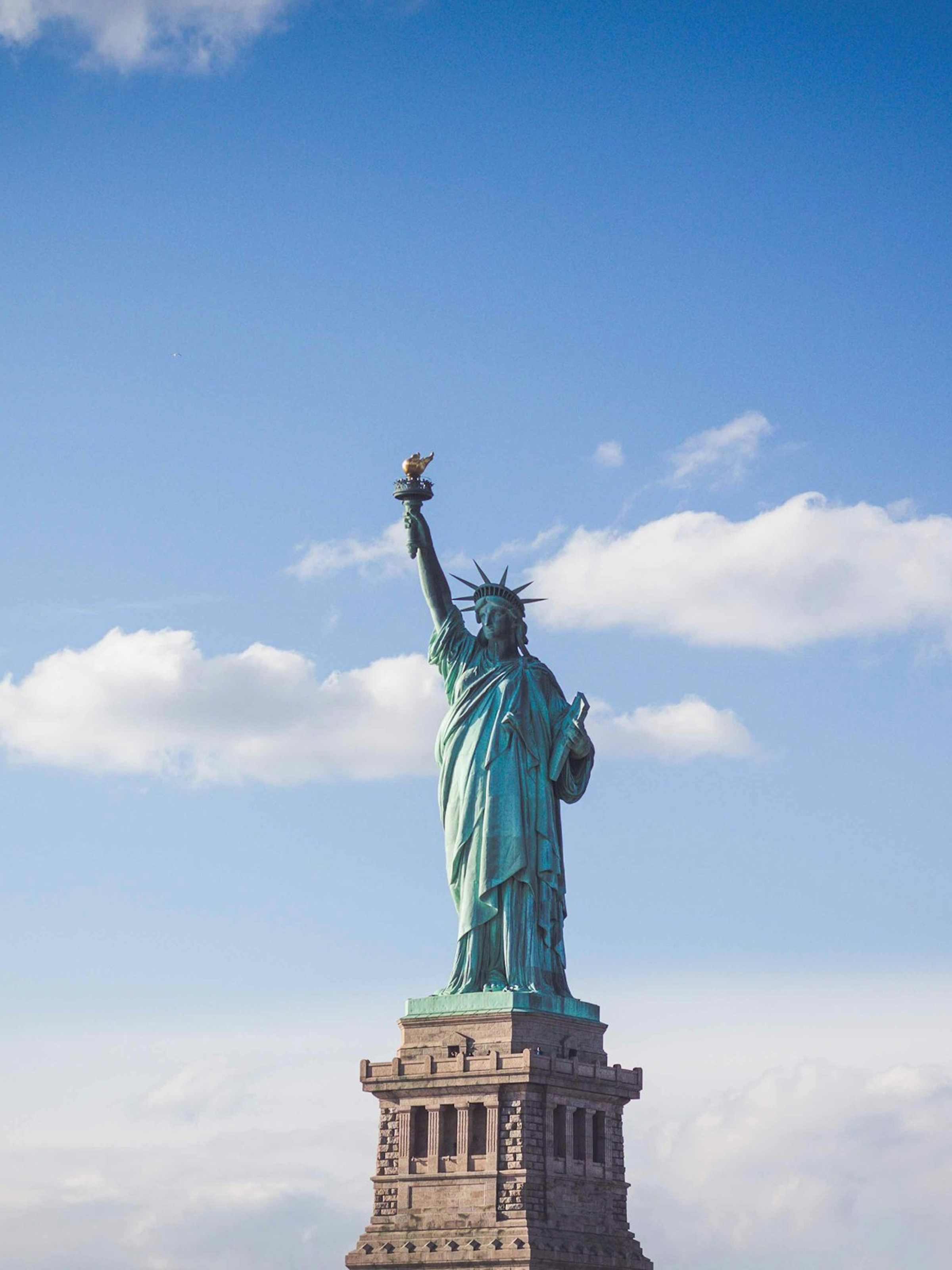 Statue of Liberty with torch raised against a blue sky with scattered clouds.