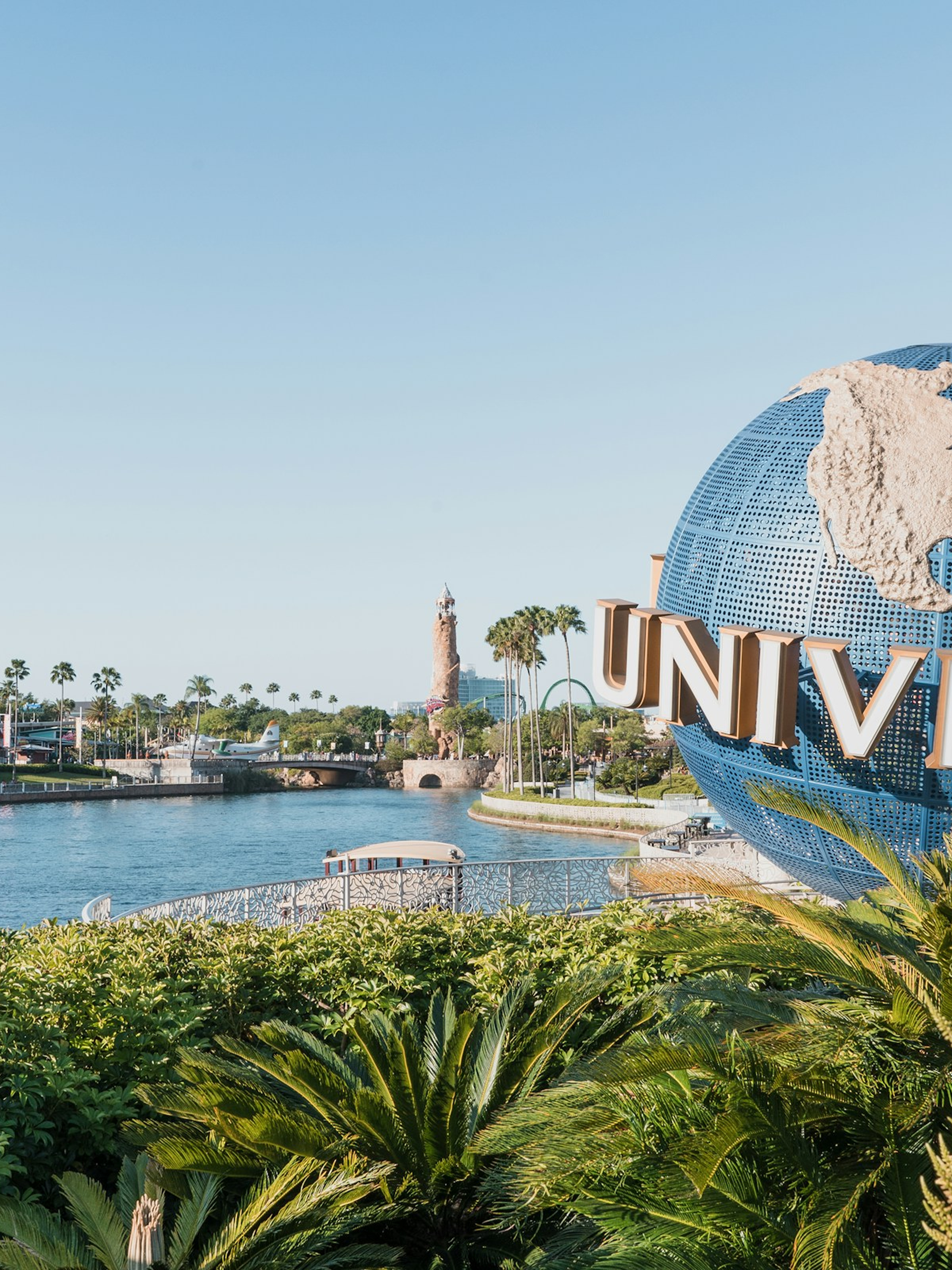 Large Universal globe sculpture partially visible with nearby river, palm trees, and clear sky.
