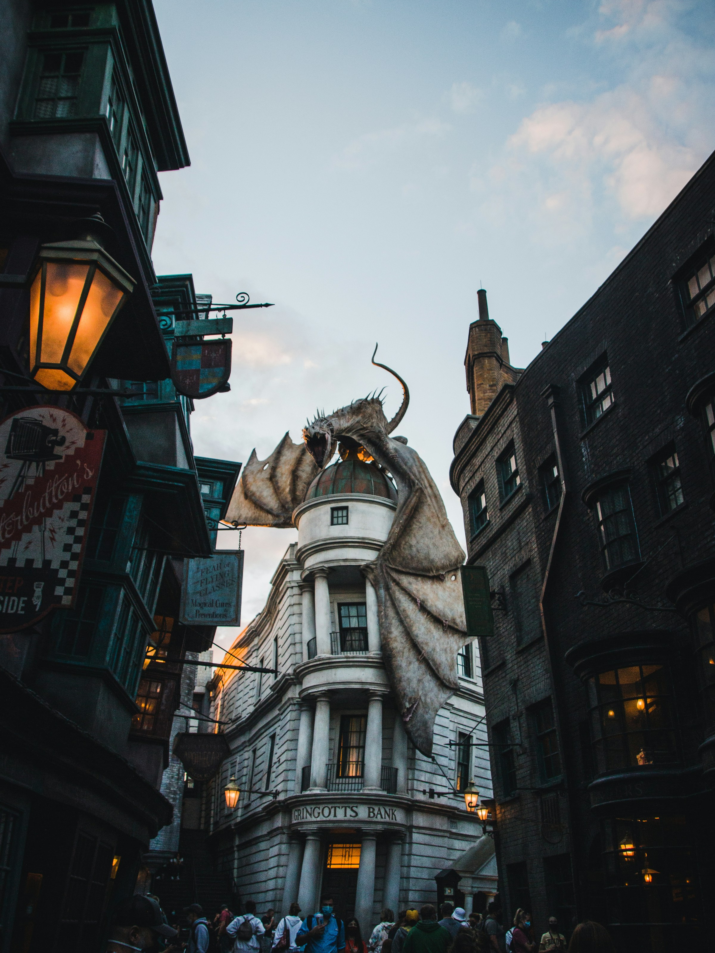 A large dragon sculpture perched atop the dome of the Gringotts Bank building with a crowd of people below.