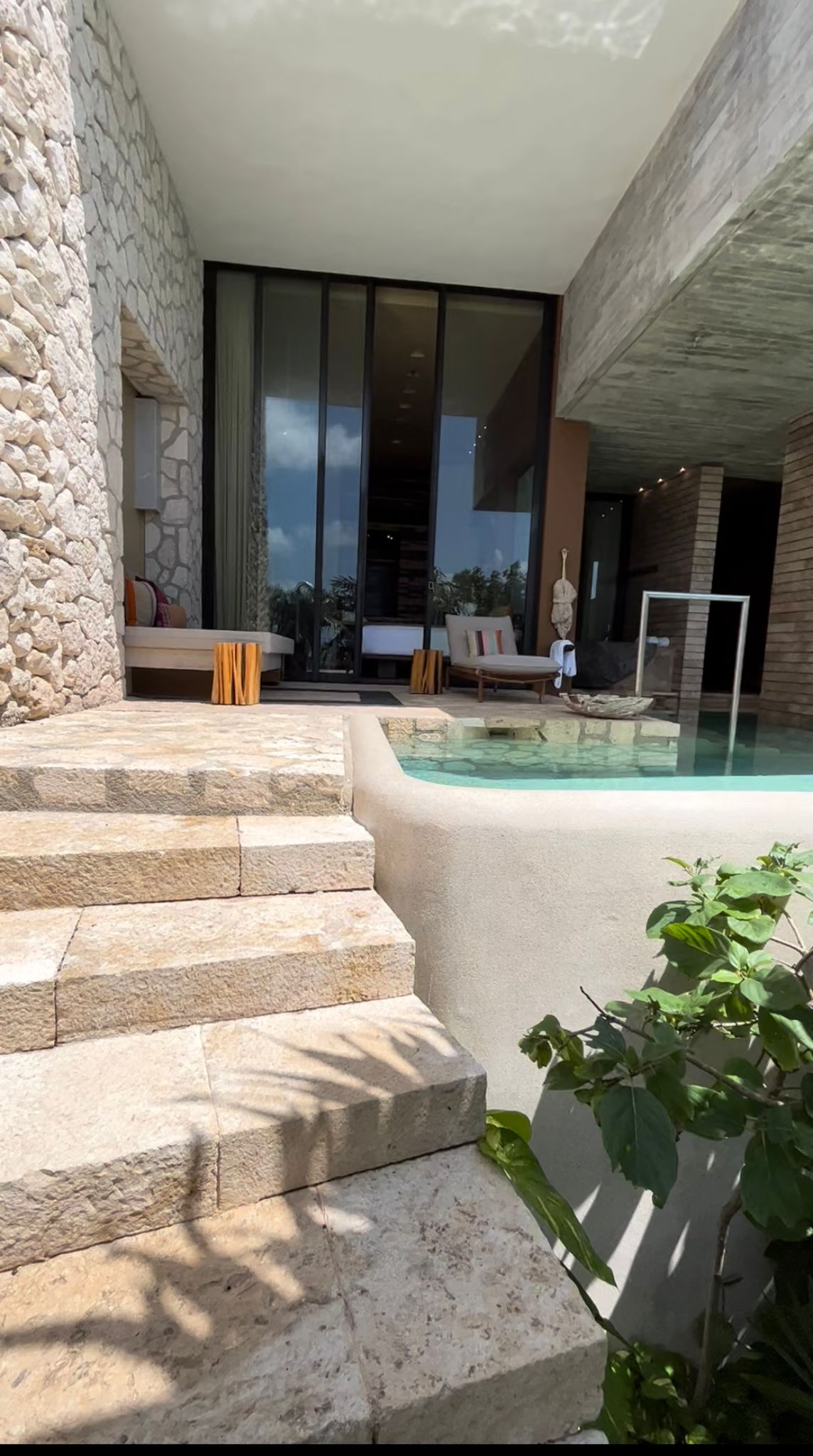 Outdoor stone steps leading to a poolside patio with lounge chairs and large glass doors reflecting the sky.