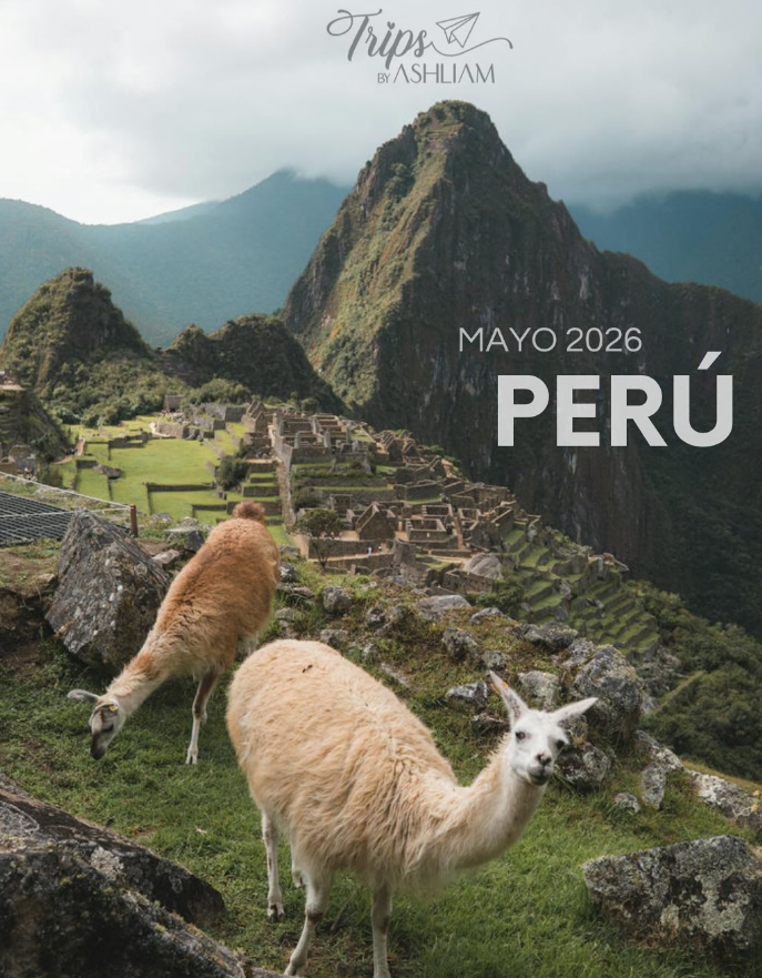 Two llamas grazing on green grass with Machu Picchu ruins and mountains in the background in Peru.