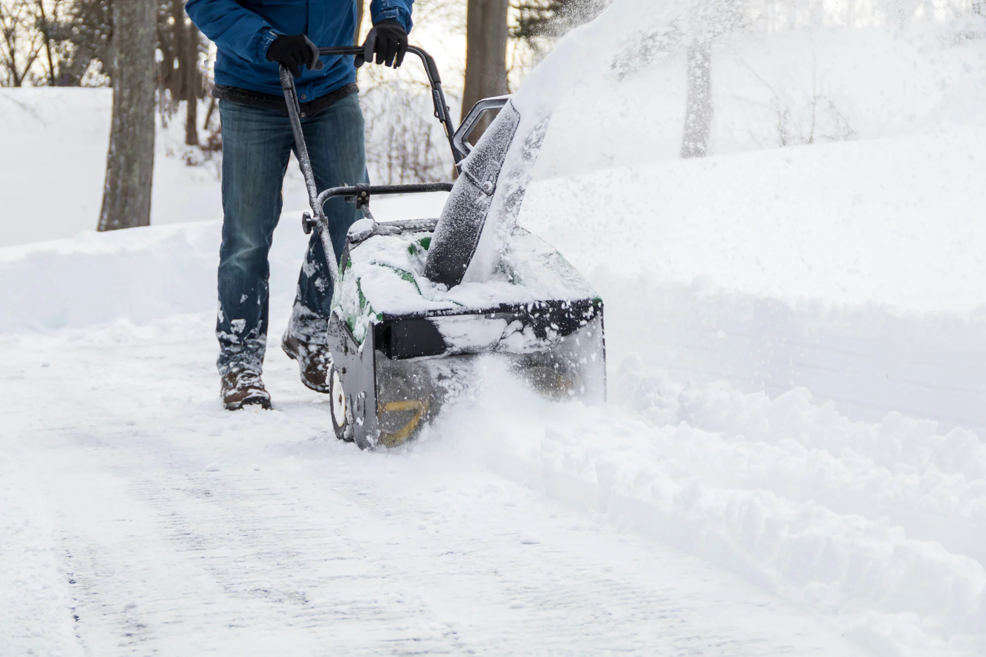 Person using a snow blower to clear a residential driveway after snowfall.