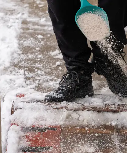 Person spreading salt on a snowy driveway to prevent ice buildup.