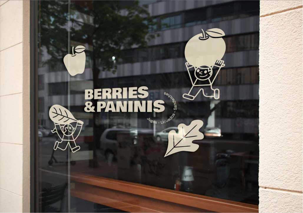 Store window with illustrations of cartoon characters holding a large apple and a leaf, with text 'BERRIES & PANINIS' and smaller text encircling it mentioning juices, smoothies, and sandwiches in Spanish.