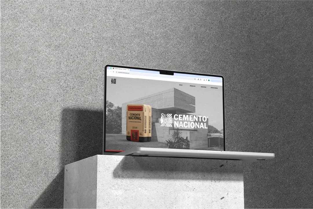 Laptop displaying Cemento Nacional website featuring a cement bag and modern concrete building, set on a concrete pedestal.