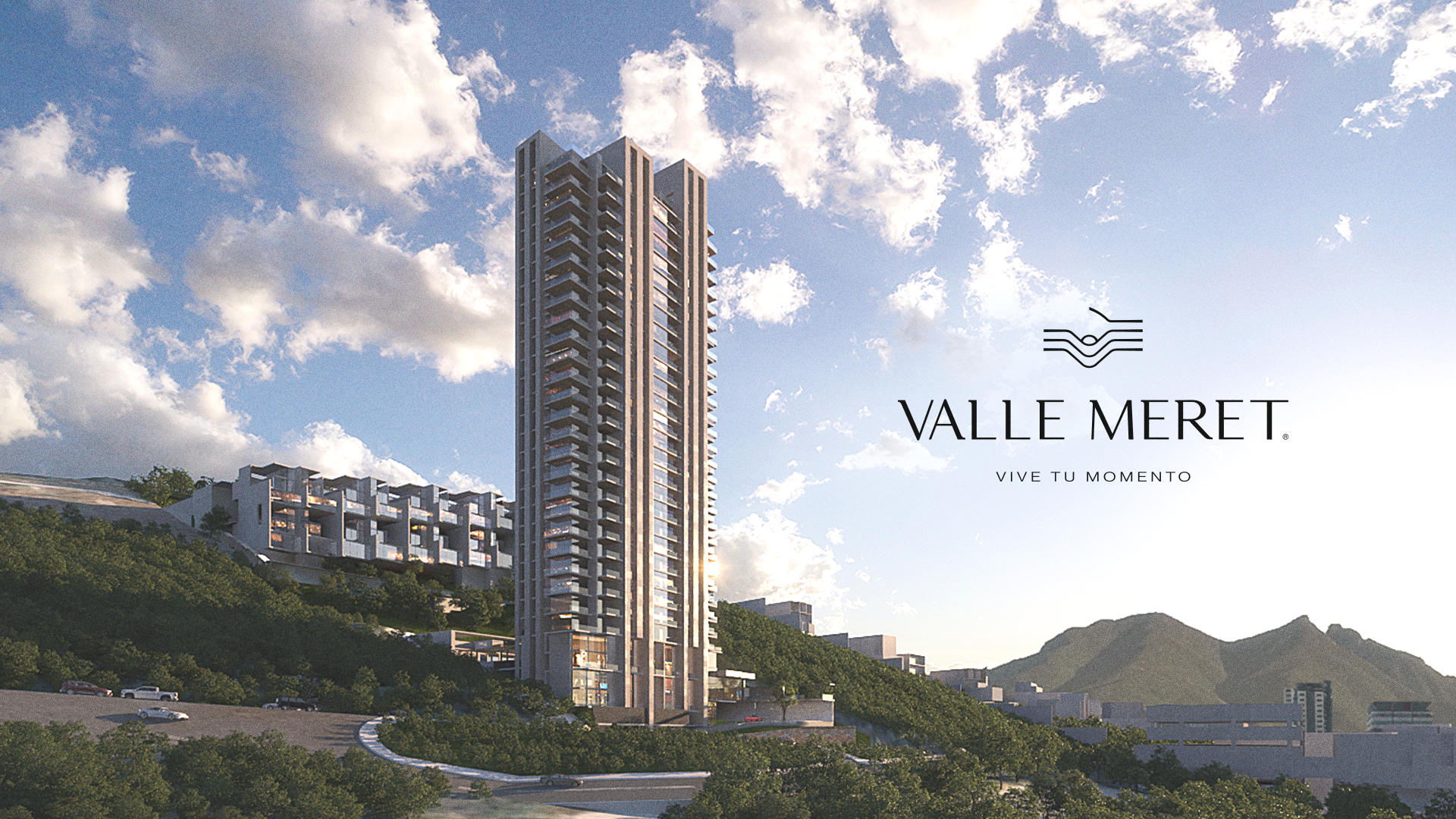 Modern high-rise residential building and smaller apartments on a green hillside under a partly cloudy sky with mountains in the background and Valle Meret logo.