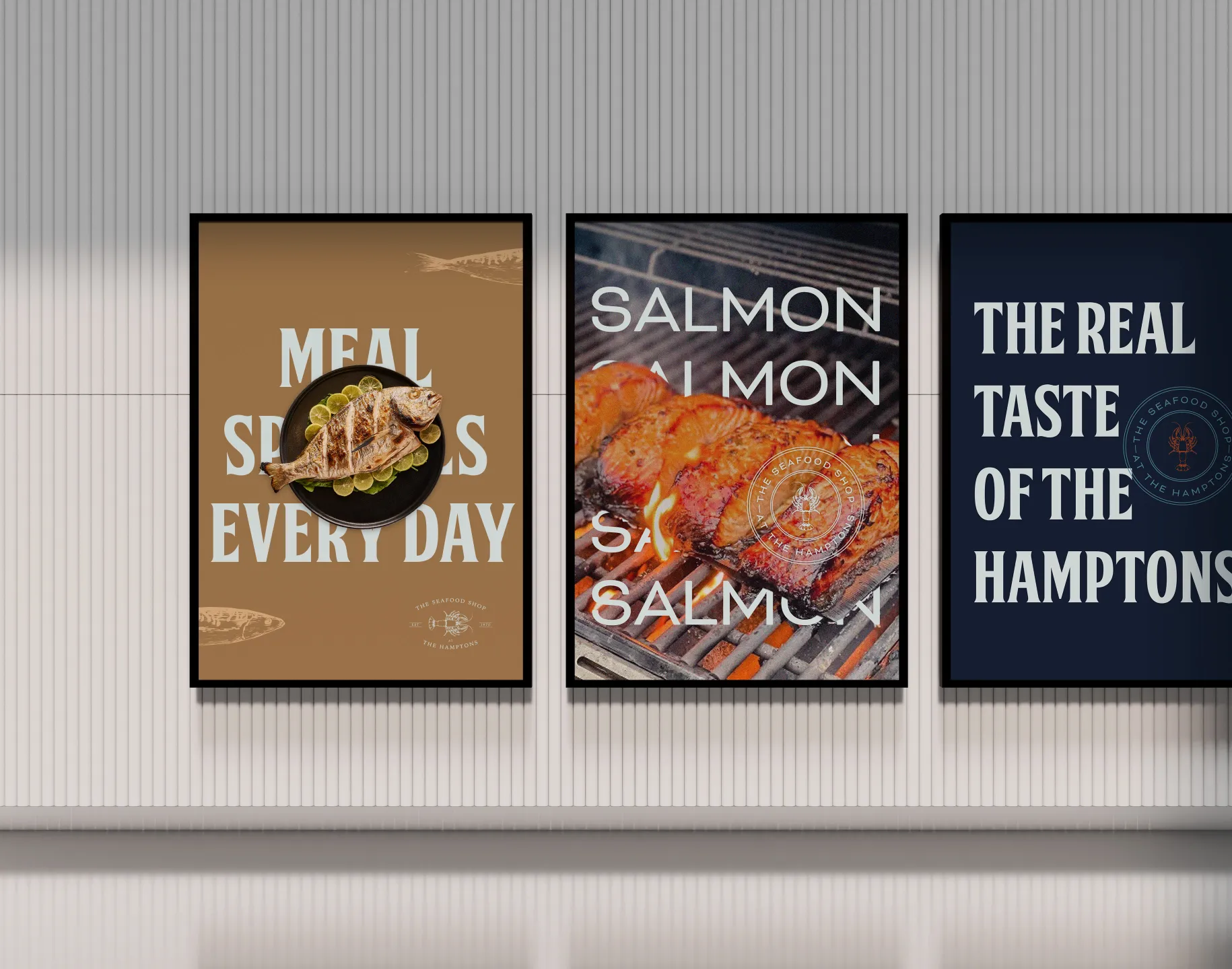 Three framed posters on a white wall: grilled fish with lime slices on plate and text 'Meal Specials Every Day,' salmon grilling with repeated text 'Salmon,' and text 'The Real Taste of The Hamptons' with seafood shop logo.