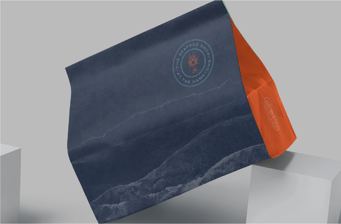 Navy blue and orange paper bag with logo featuring a lobster and text 'The Seafood Shop - At the Hamptons'.