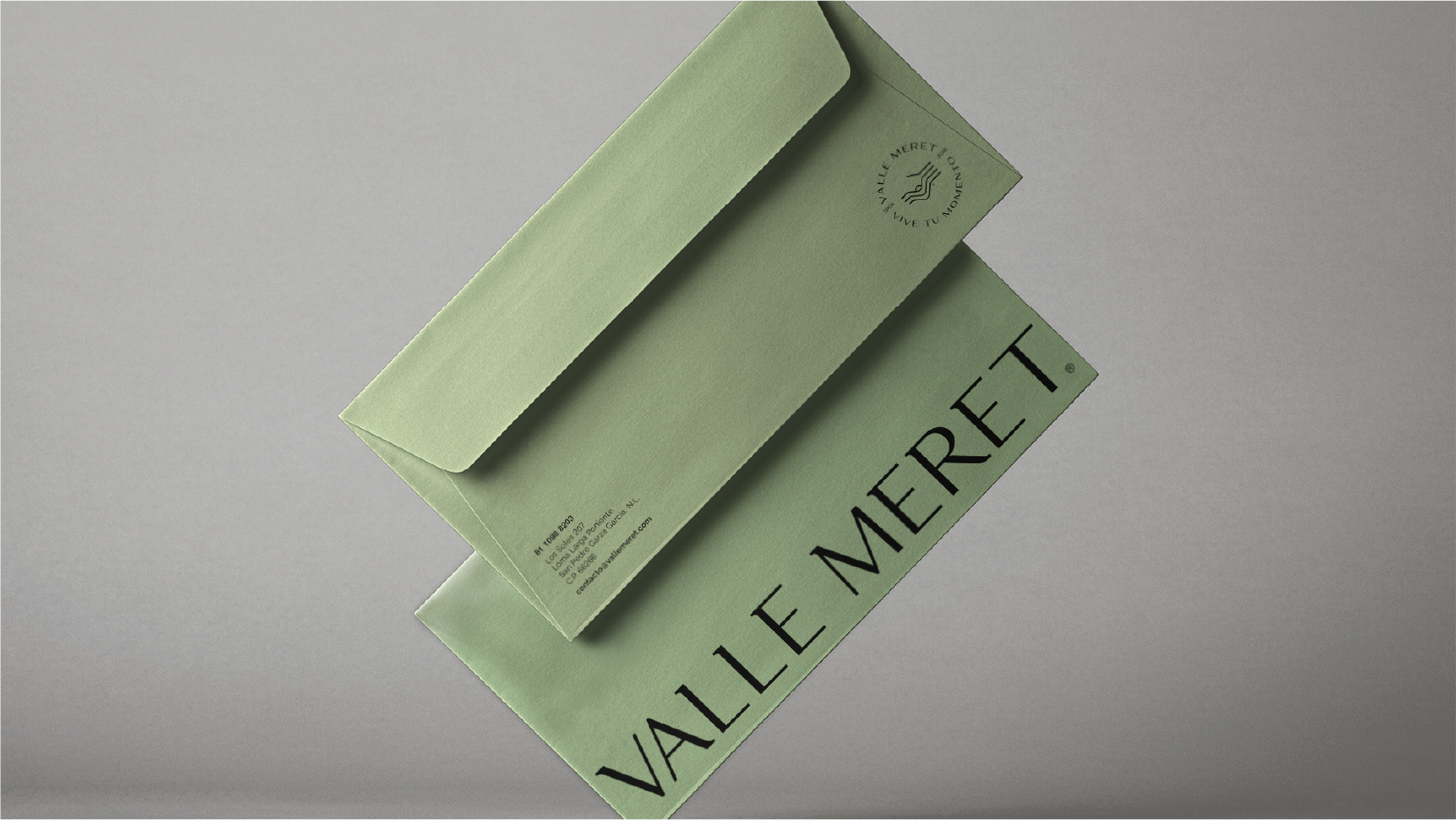 Two olive green envelopes stacked diagonally, with VALLE MERET printed in black on the bottom envelope and contact details on the top one.