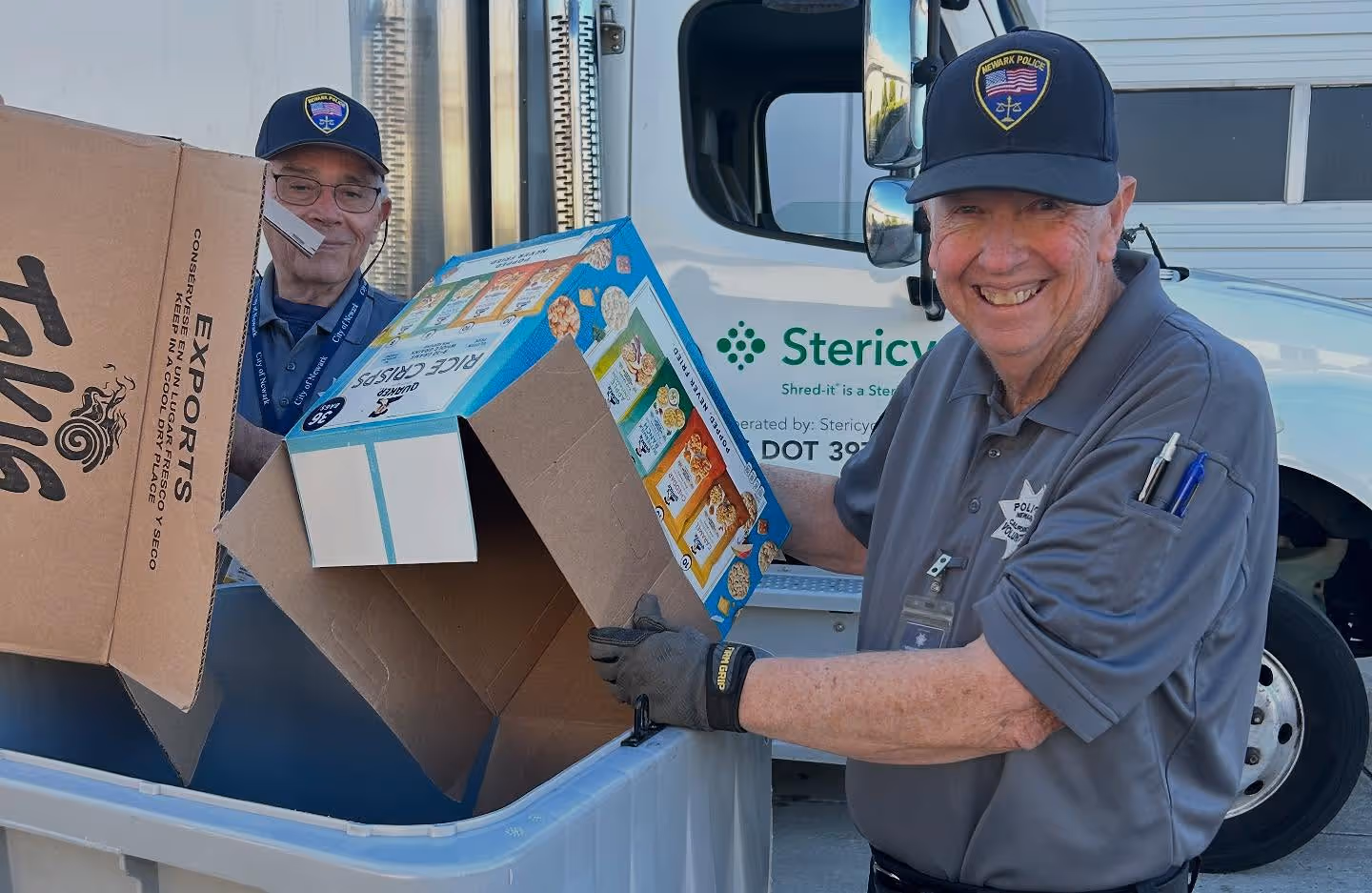 Two Newark Police Association members smiling while participating in a community recycling effort with cardboard boxes