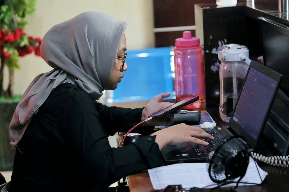 woman multitasking with phone and laptop in office