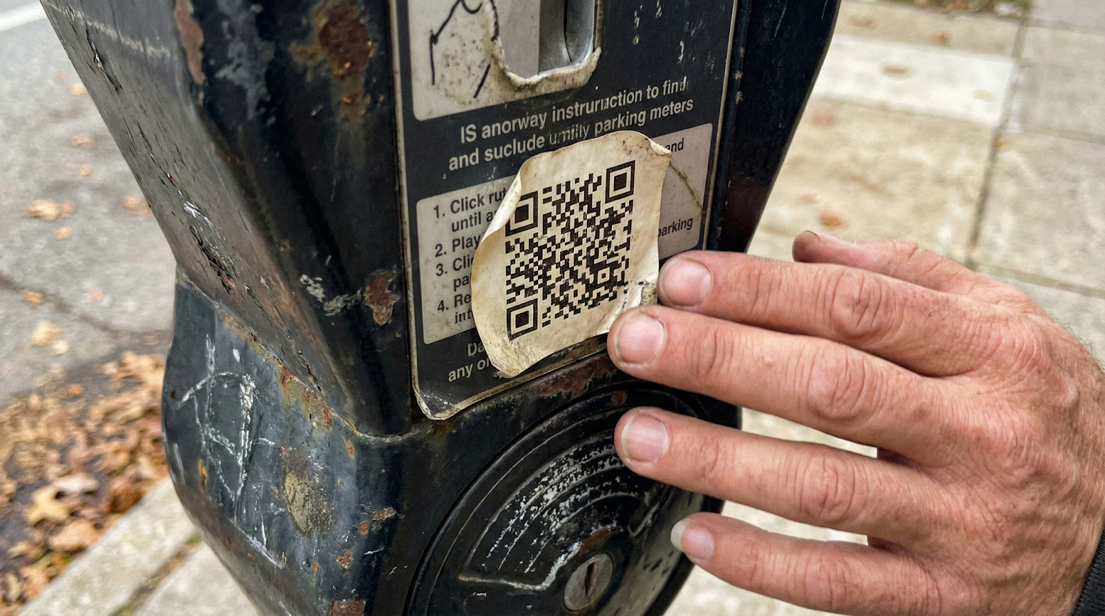 Close-up of suspicious QR code sticker peeling at edges on parking meter