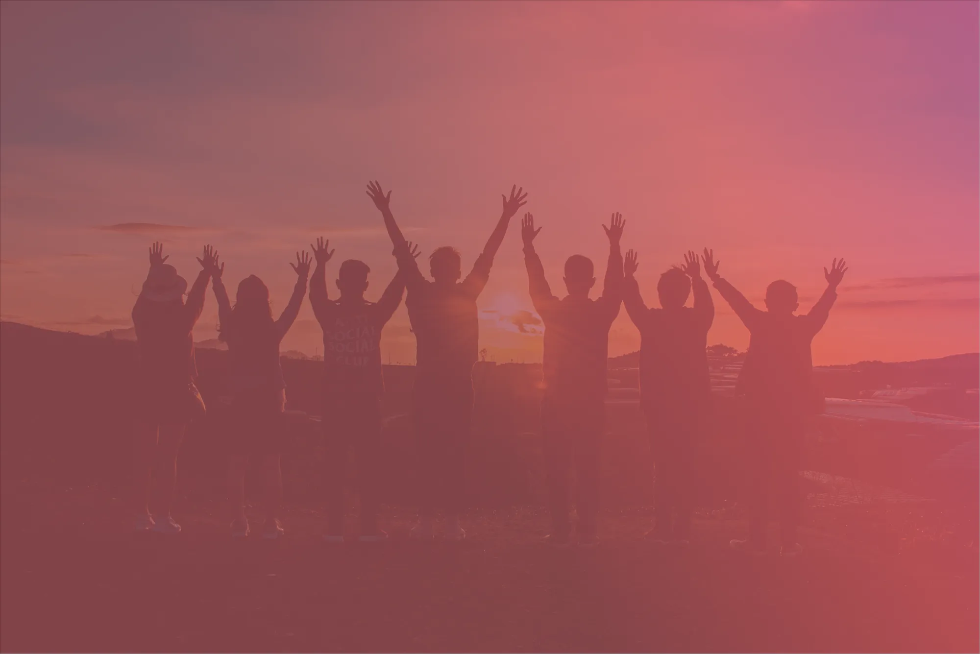 Silhouettes of seven people standing side by side with arms raised against a sunset background.