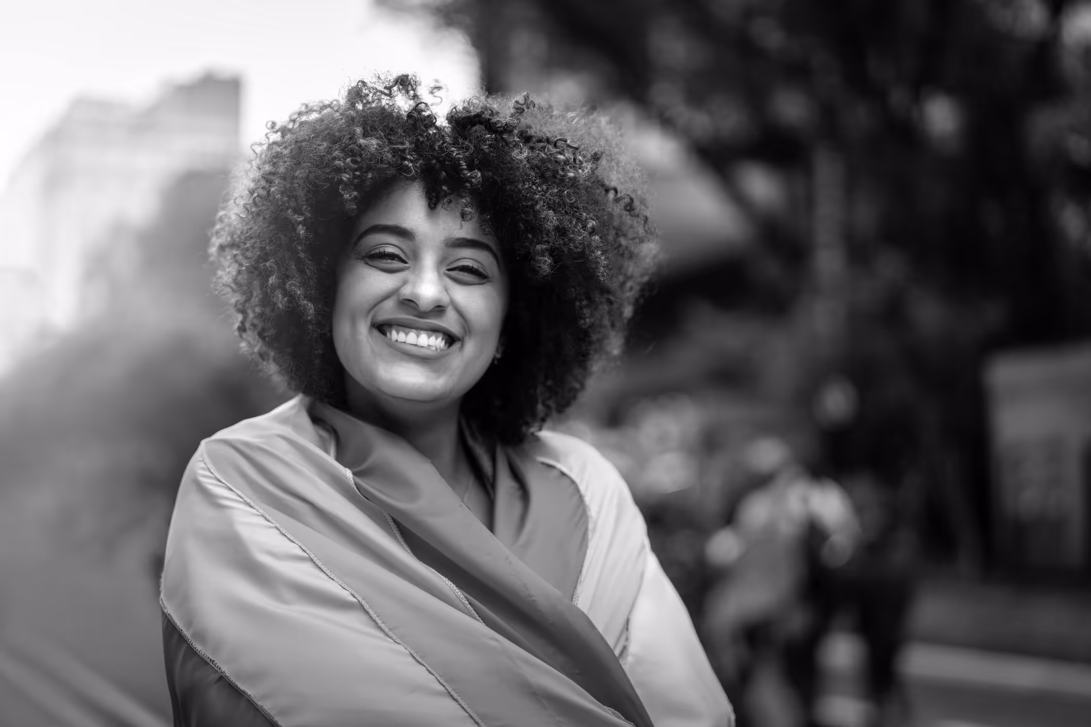 A queer person wrapped in a rainbow flag smiles at the camera