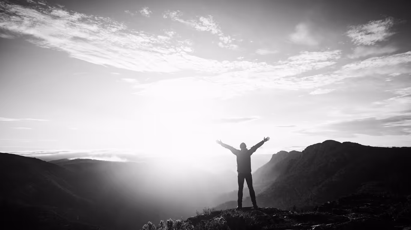 A young person outstretches their arms in the morning sun while hiking in the mountains