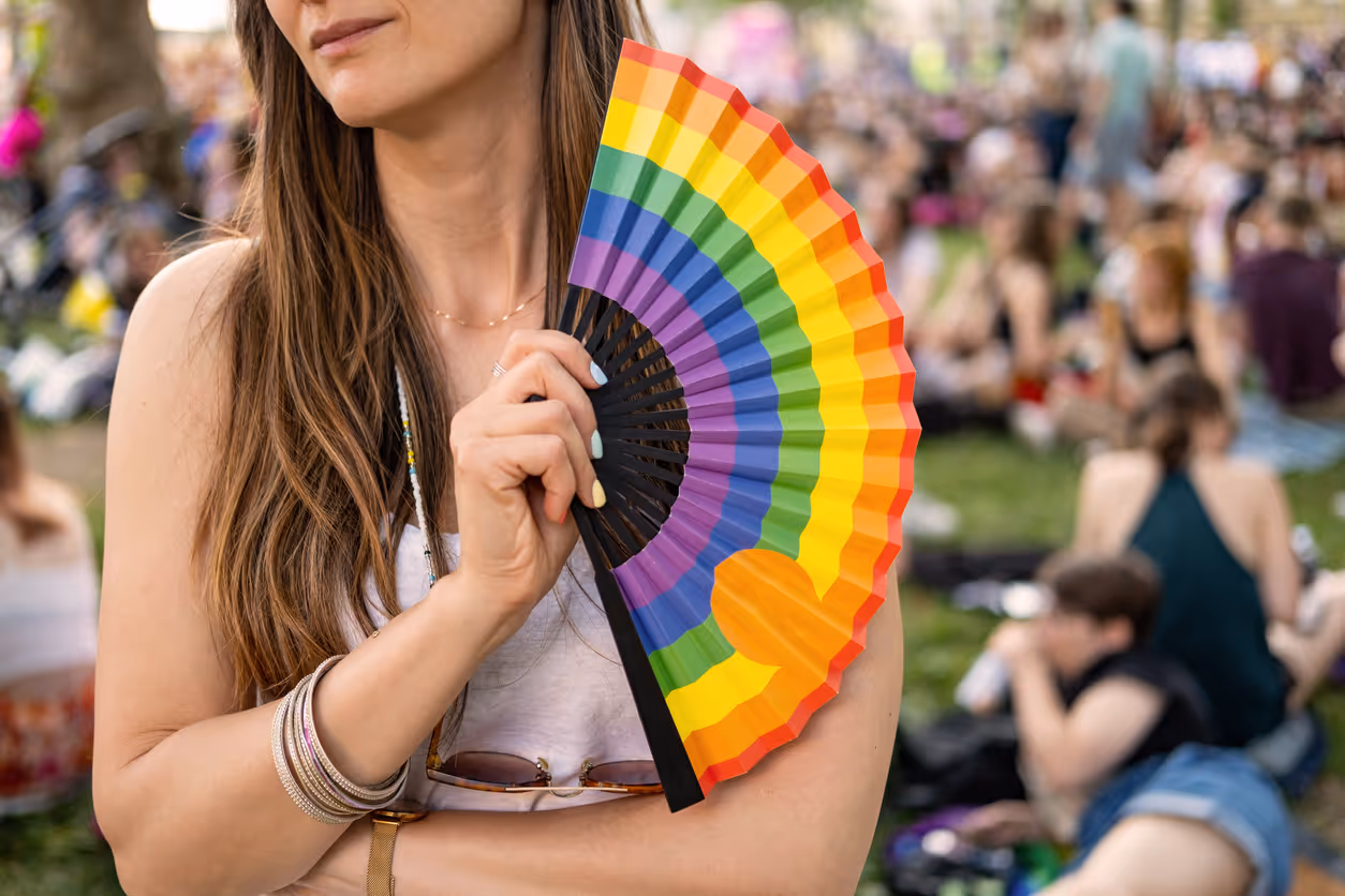 Person holding a rainbow-coloured hand fan at an outdoor Pride festival