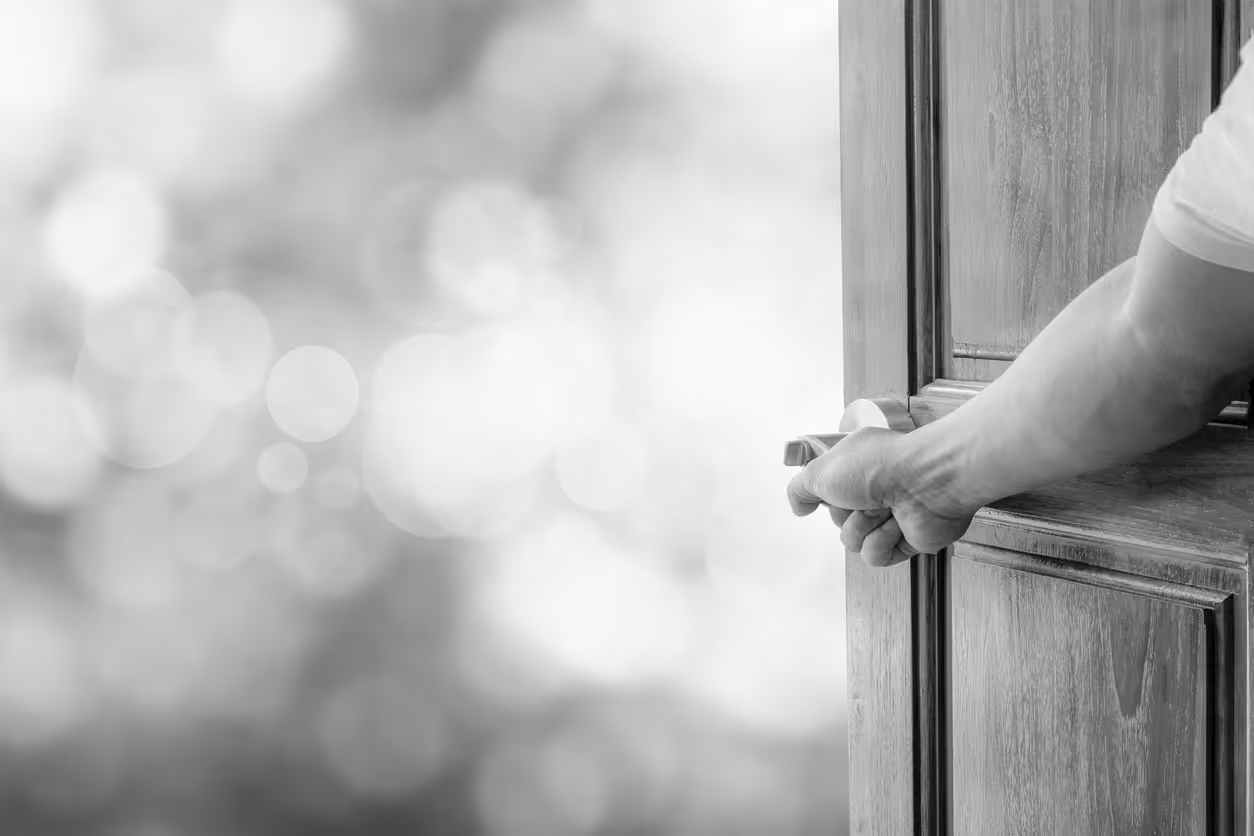 A hand touches a doorknob to open the door to the outside world