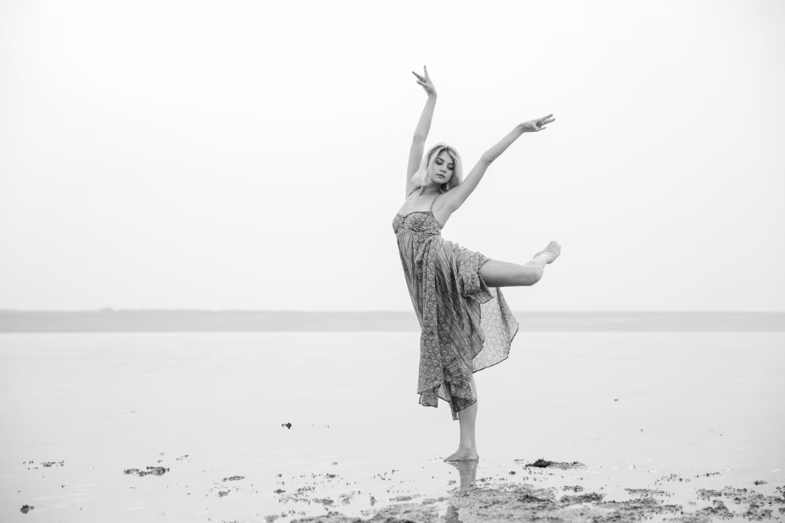 A feminine-presenting person dances gracefully on the beach.
