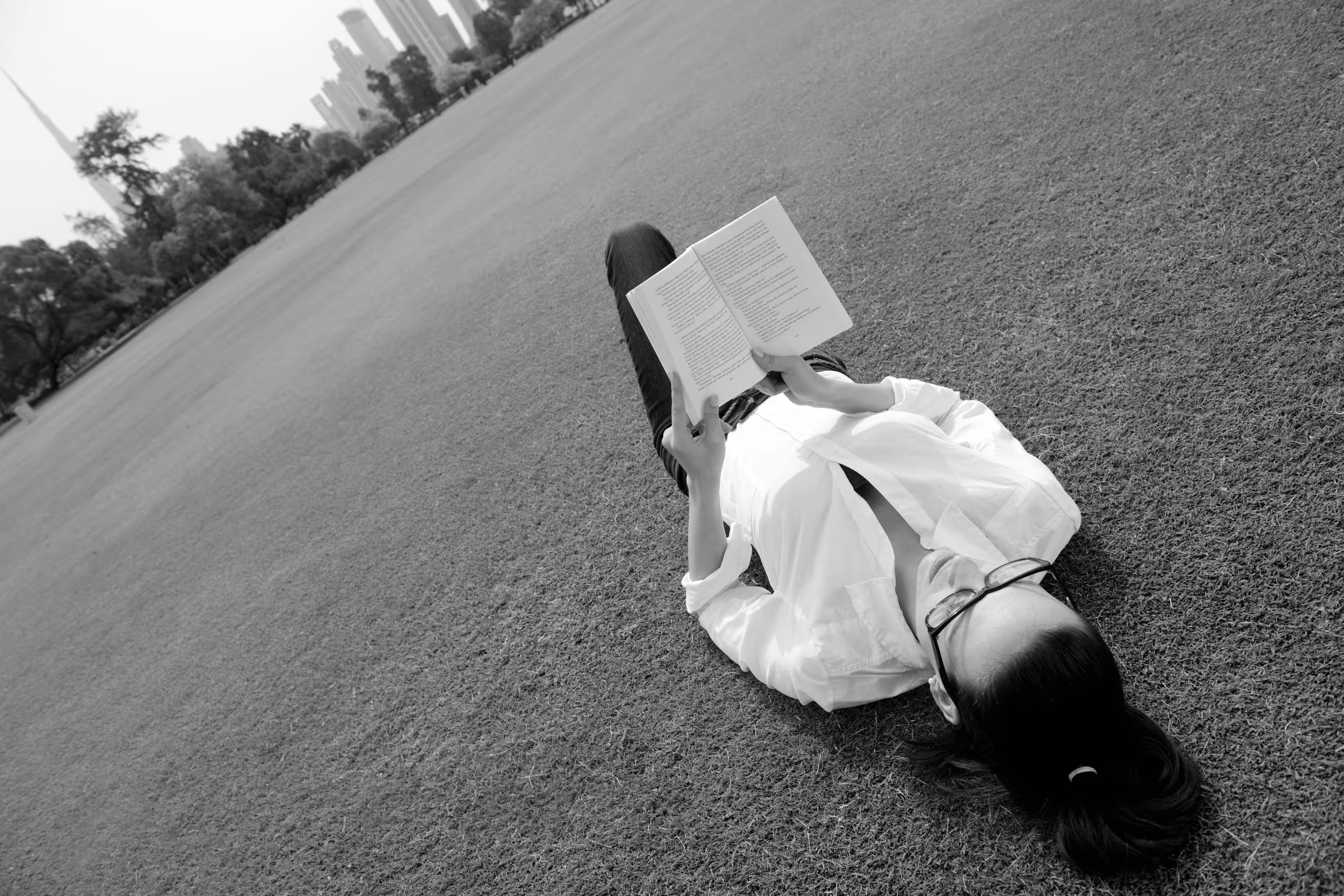 Nonbinary person reading a book while lying in the grass