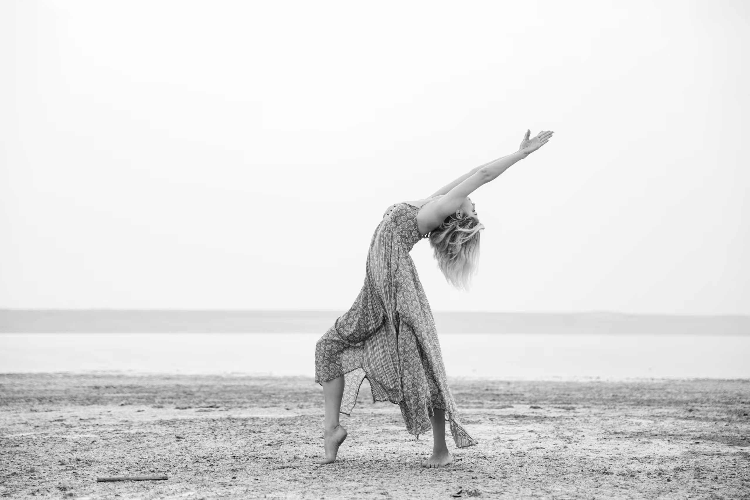 A feminine-presenting person dances gracefully on the beach.