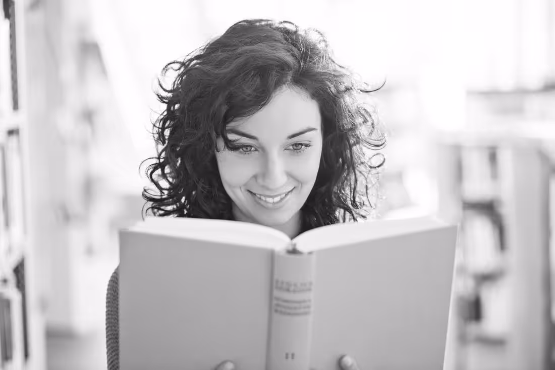 An adult with a smile on her face reads the book What I Mean When I Say I'm Autistic by Annie Kotowicz