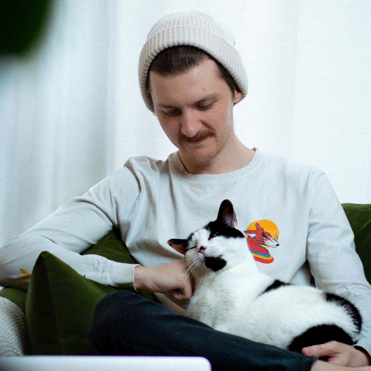 Portrait of a man wearing white sitting on a green chair with a white and black cat
