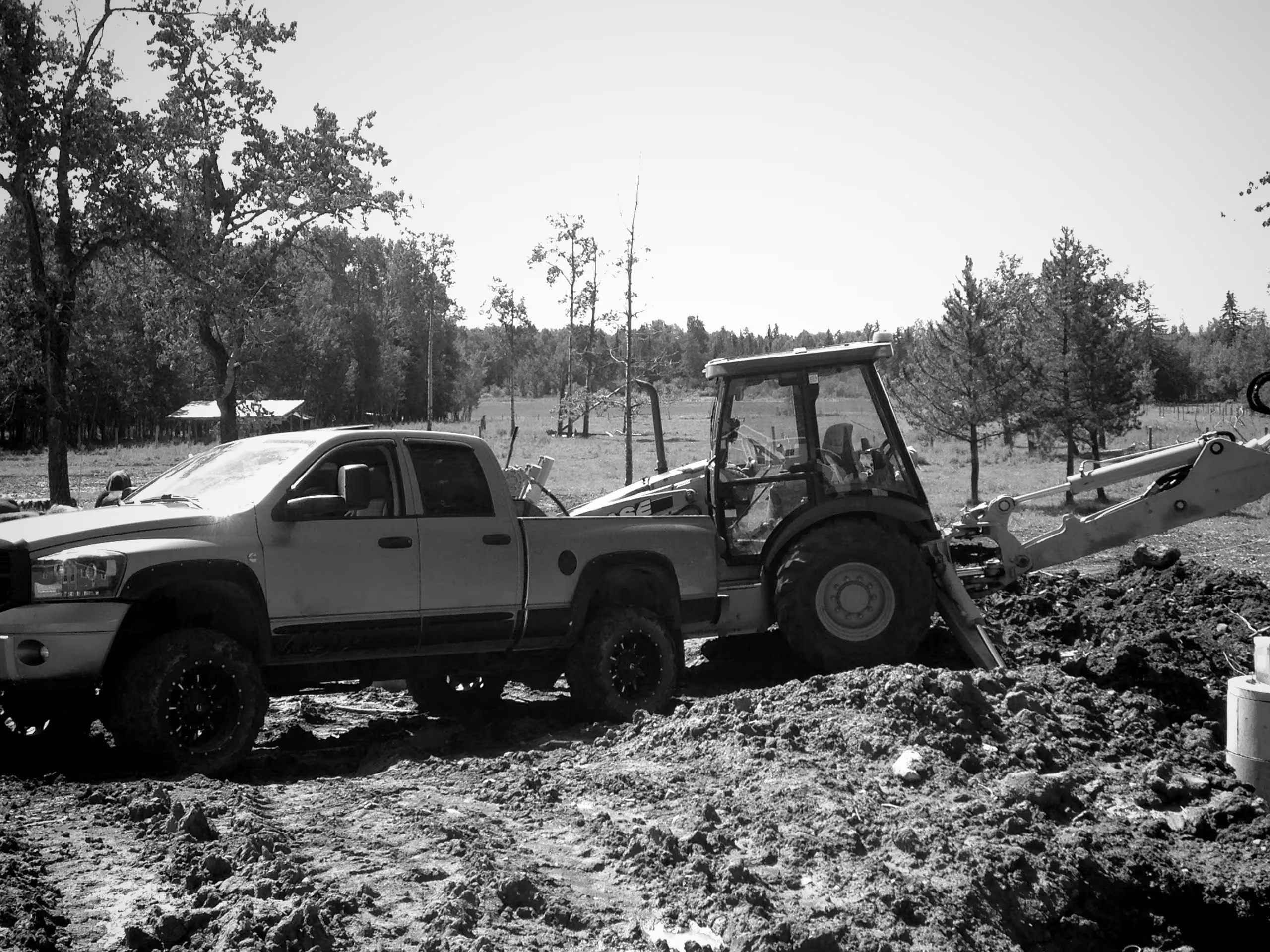 Pickup truck stuck in muddy terrain being assisted by a backhoe loader.