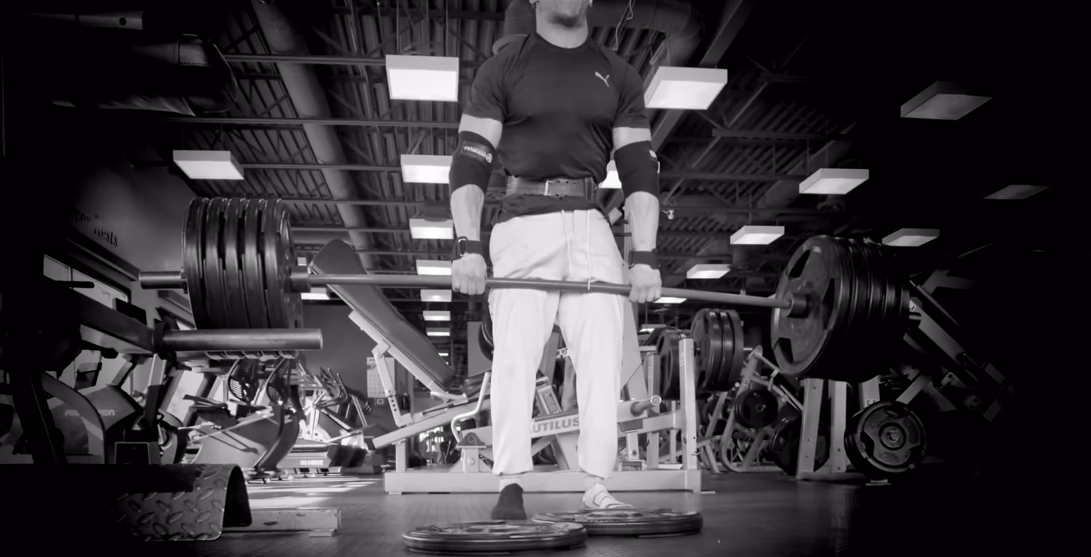 Man in gym gear performing a deadlift with a heavily loaded barbell in a gym setting.