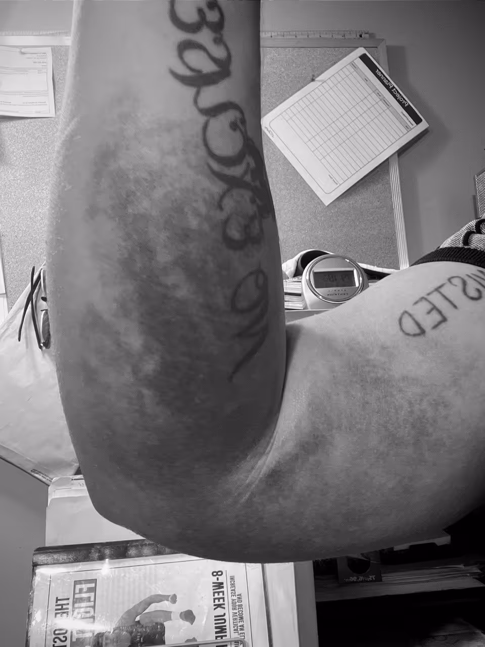 Black and white close-up of a flexed tattooed arm with visible veins and muscles in an indoor setting.