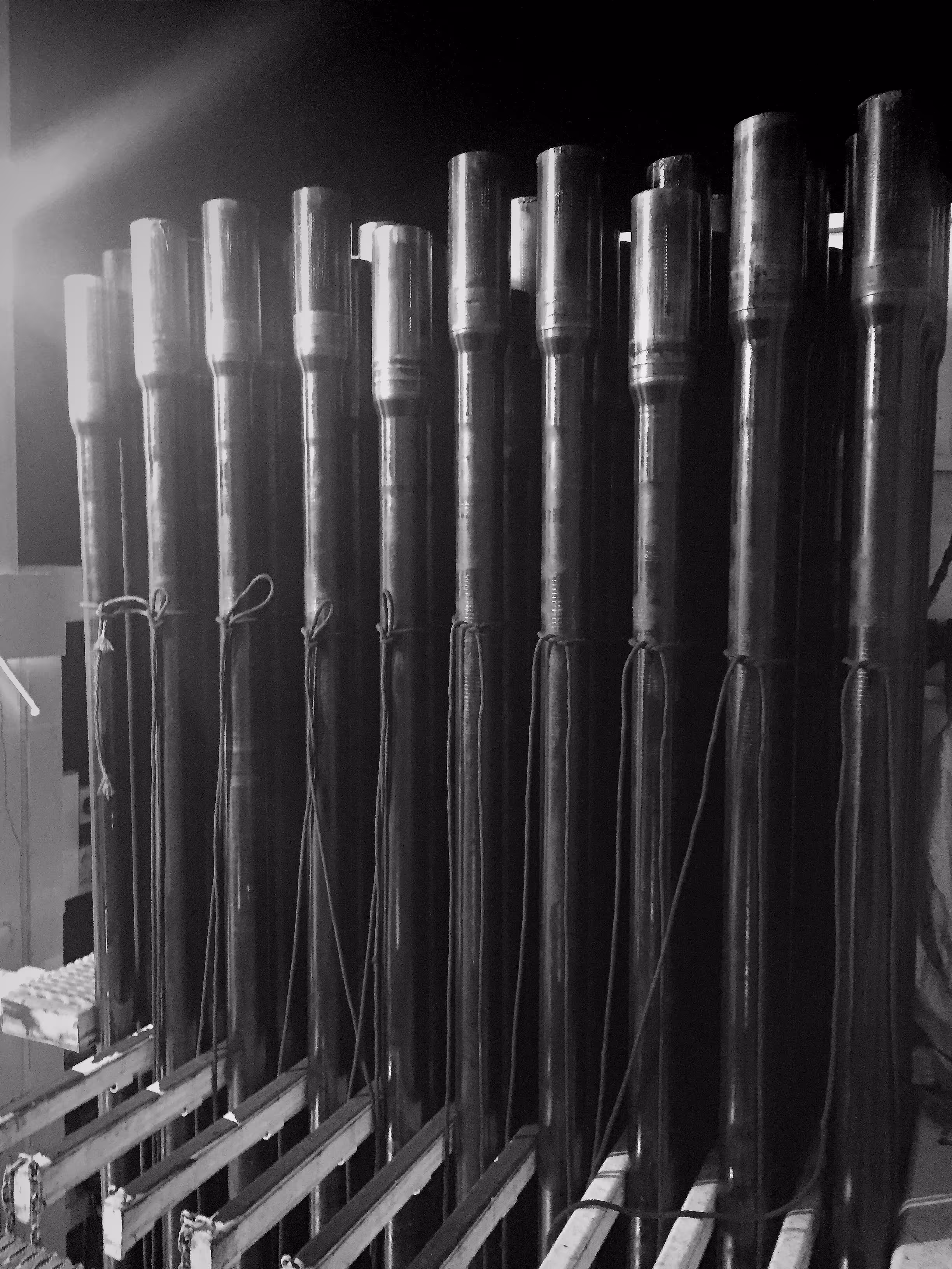 Close-up of a row of large vertical metal pipes with strings attached, likely part of a musical instrument or mechanical installation.