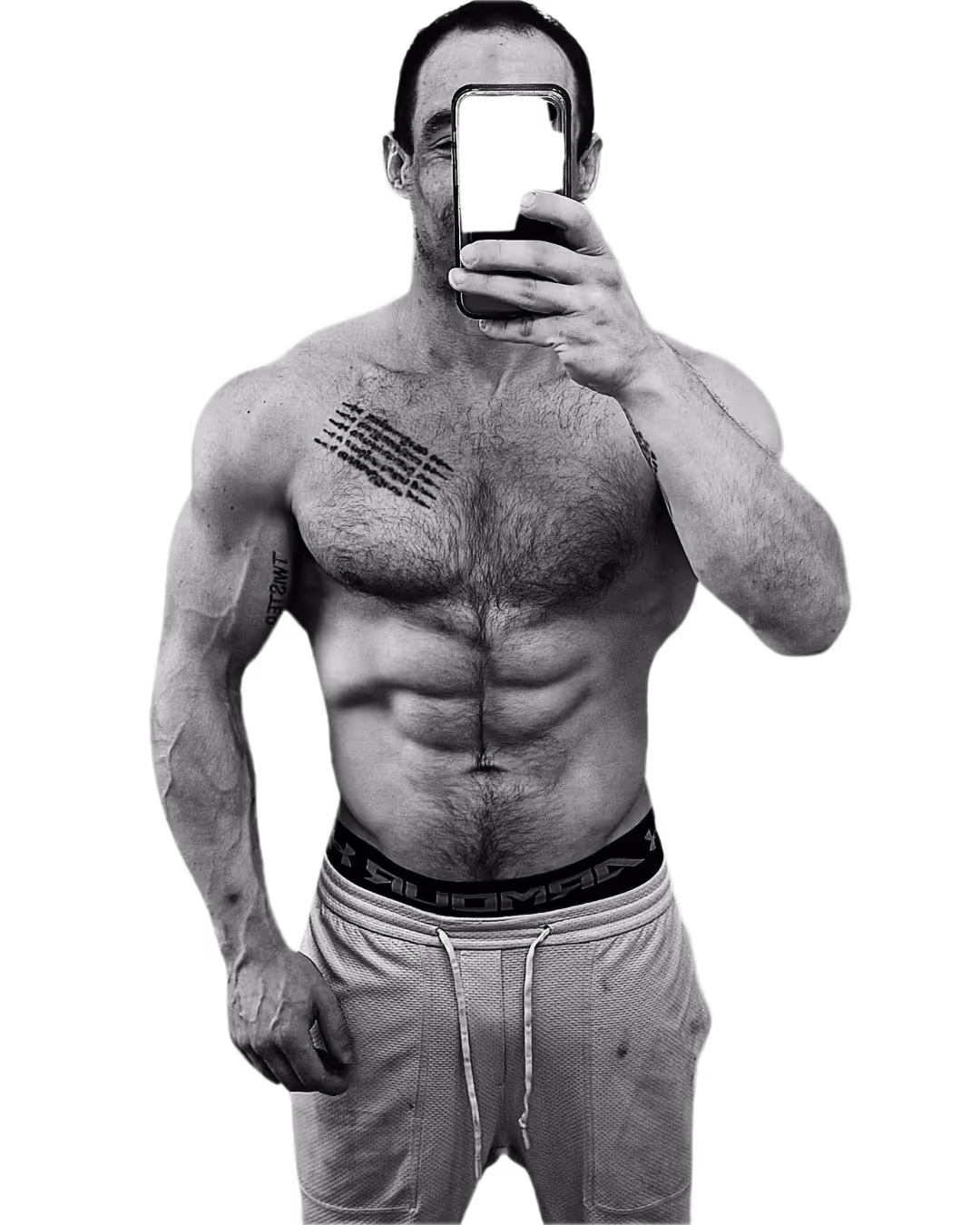 Shirtless muscular man taking a selfie with a smartphone, showing chest tattoos and wearing drawstring pants.