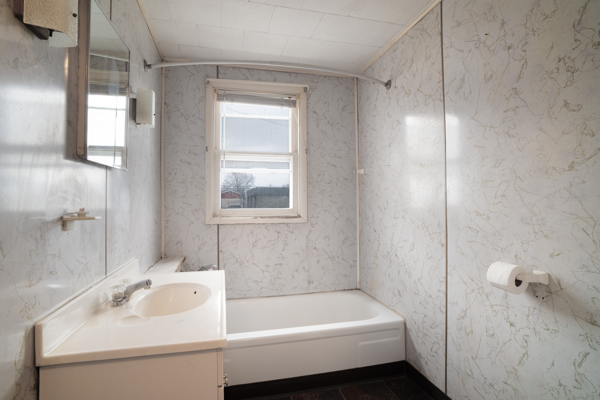 Small bathroom with a bathtub, a sink with a faucet, a window, patterned light-colored walls, and a mounted toilet paper holder.