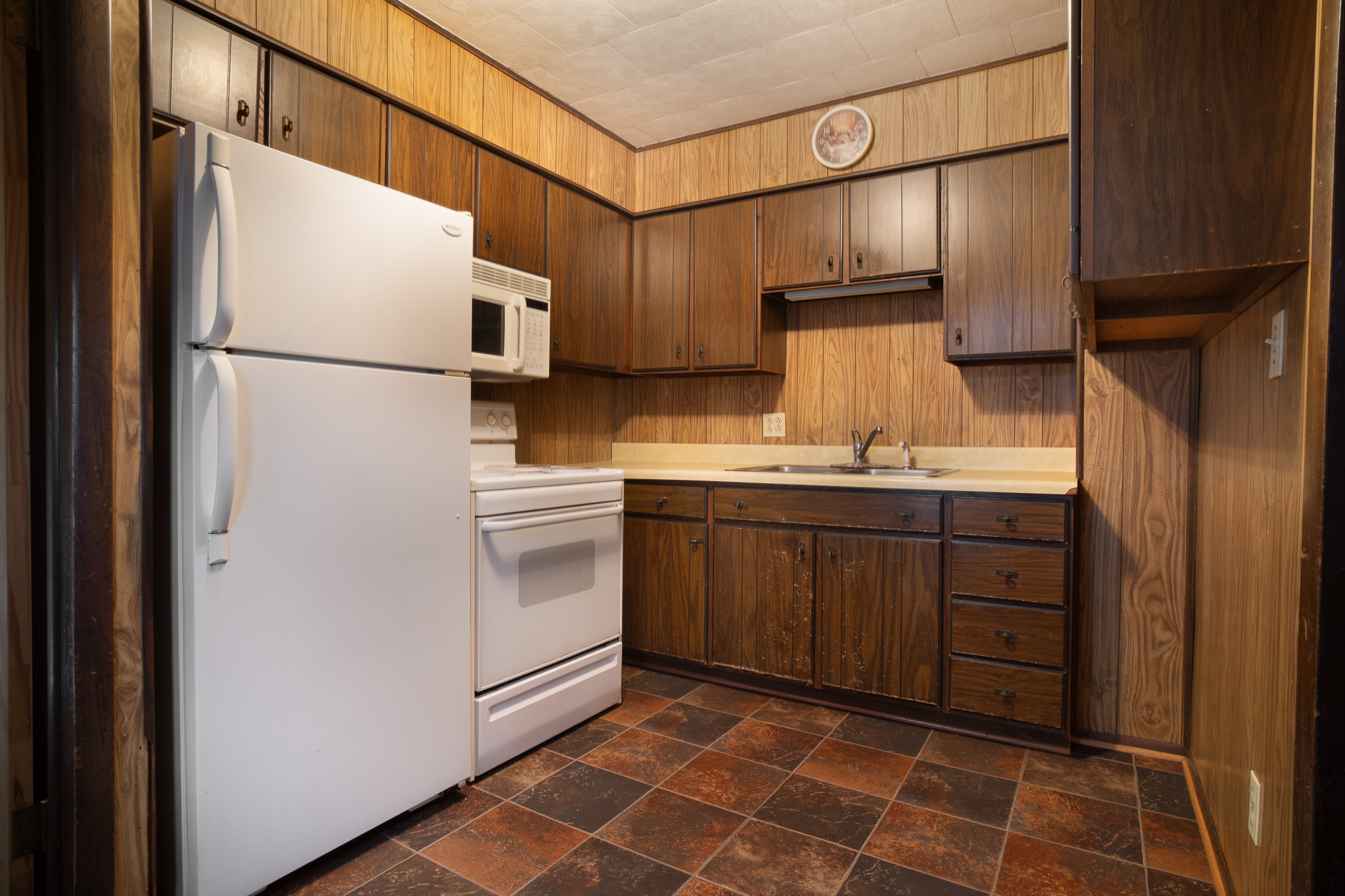 Kitchen with white refrigerator, stove, microwave, dark wood cabinets, beige countertop, and tiled floor.