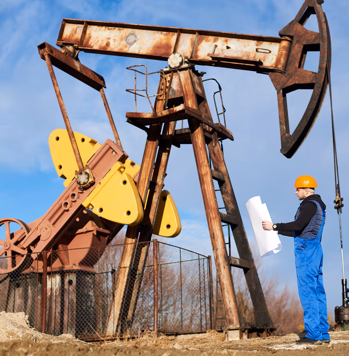 A man in a hard hat standing next to an oil pump.