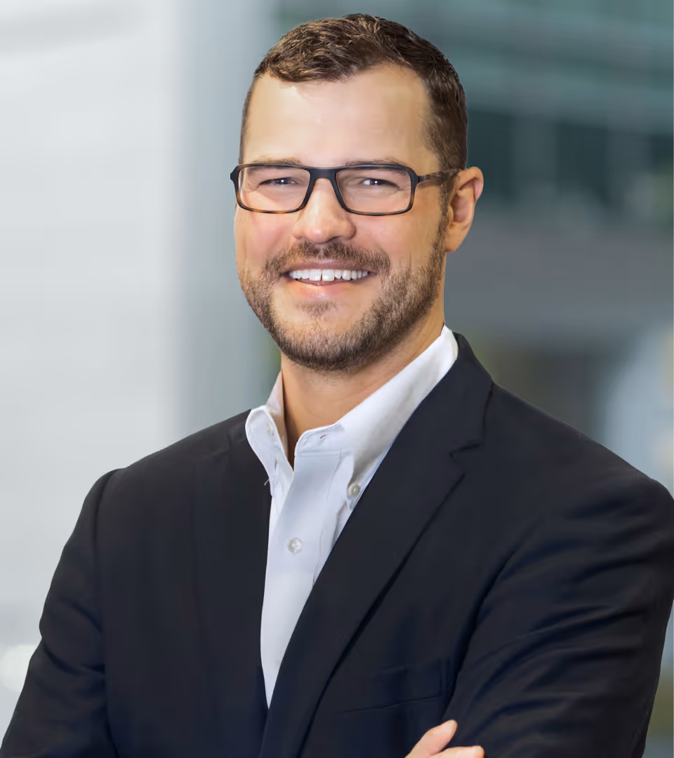 Smiling man with short brown hair, glasses, and a trimmed beard wearing a dark blazer over a white shirt.
